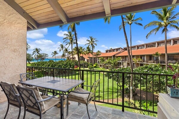 A balcony with a table and chairs, overlooking a pool and a building with palm trees.