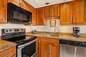 A kitchen with wooden cabinets, a microwave, stove, dishwasher, and granite countertops.