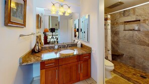 Un baño con encimera de granito, armarios de madera, un espejo grande y una ducha con paredes de piedra.