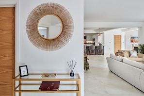 Un salon moderne avec un miroir rond, une table basse en verre sur laquelle reposent un livre et des clés, et un canapé.