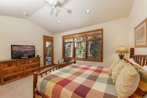 A bedroom with a bed, a television, a dresser, and a window with a view of trees.