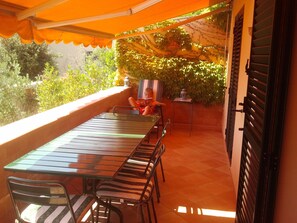 Pátio externo com mesa e cadeiras, cercado por vegetação e piso de azulejos.