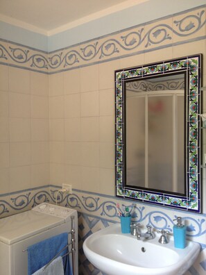 Um banheiro com pia branca, espelho com moldura decorativa e máquina de lavar.
