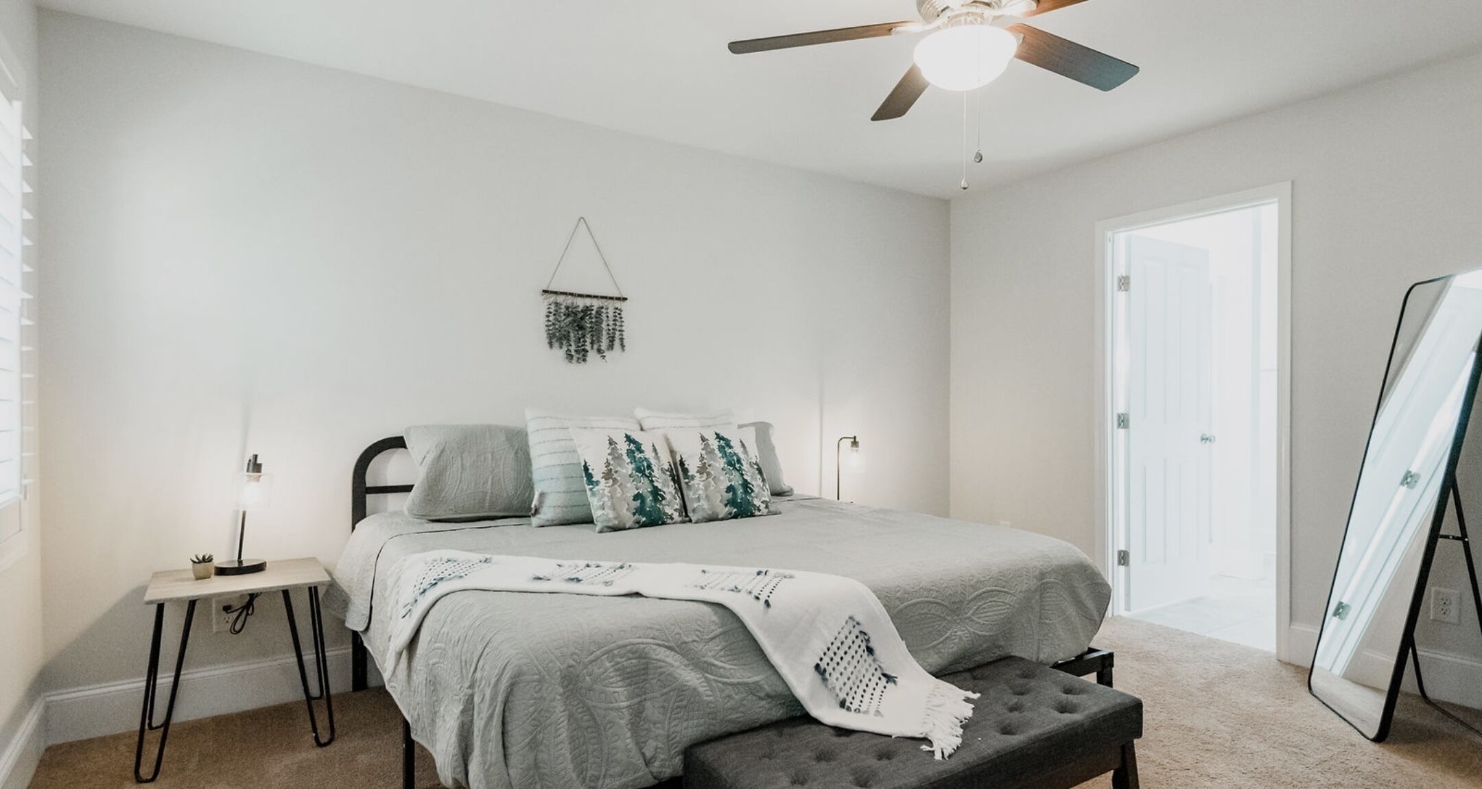 Une chambre à coucher avec un lit, des tables de chevet, un ventilateur de plafond et une porte.