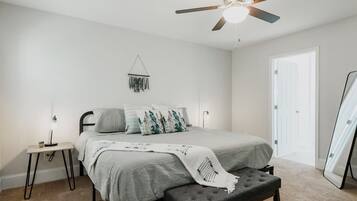 Une chambre à coucher avec un lit, des tables de chevet, un ventilateur de plafond et une porte.