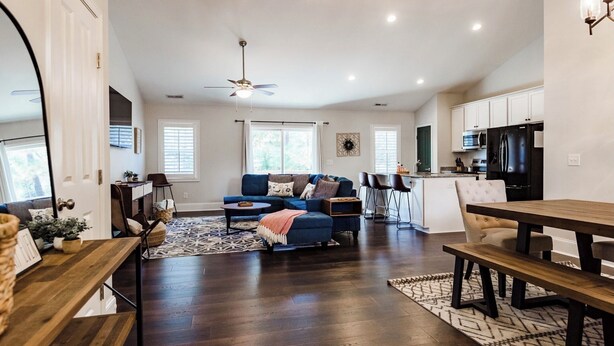 A spacious living room with a blue sofa, a dining area with a wooden table, and a kitchen with modern appliances. - A Home in One ⛳️ Sleeps 10 & 🎱 Table! (West End)