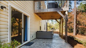 A covered patio with stone flooring, a wicker sofa, and a wooden deck. - A Home in One ⛳️ Sleeps 10 & 🎱 Table! (West End)