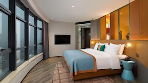 Een moderne hotelkamer met een groot bed, een televisie en uitzicht op de stad door middel van grote raampartijen.