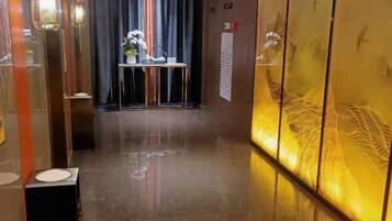 A hallway with a reflective floor, a table with flowers, and a wall with a decorative pattern.