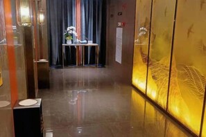 A hallway with a reflective floor, a table with flowers, and a wall with a decorative pattern.