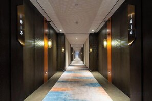 Ein Hotelgang mit einer langen, schmalen Diele, Wandleuchten und Stockwerken.