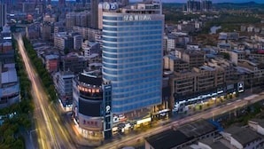 Een hoog hotel met meerdere verdiepingen, omgeven door andere gebouwen, en een drukke straat met verkeer.