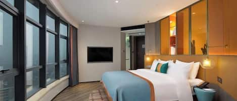 A modern hotel room with a large bed, a TV, and a view of the city through floor-to-ceiling windows.