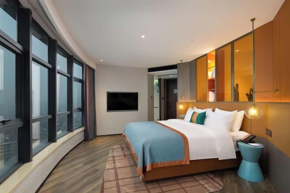 Une chambre d’hôtel moderne dotée d’un grand lit, d’une télévision et offrant une vue sur la ville grâce à de grandes fenêtres du sol au plafond.