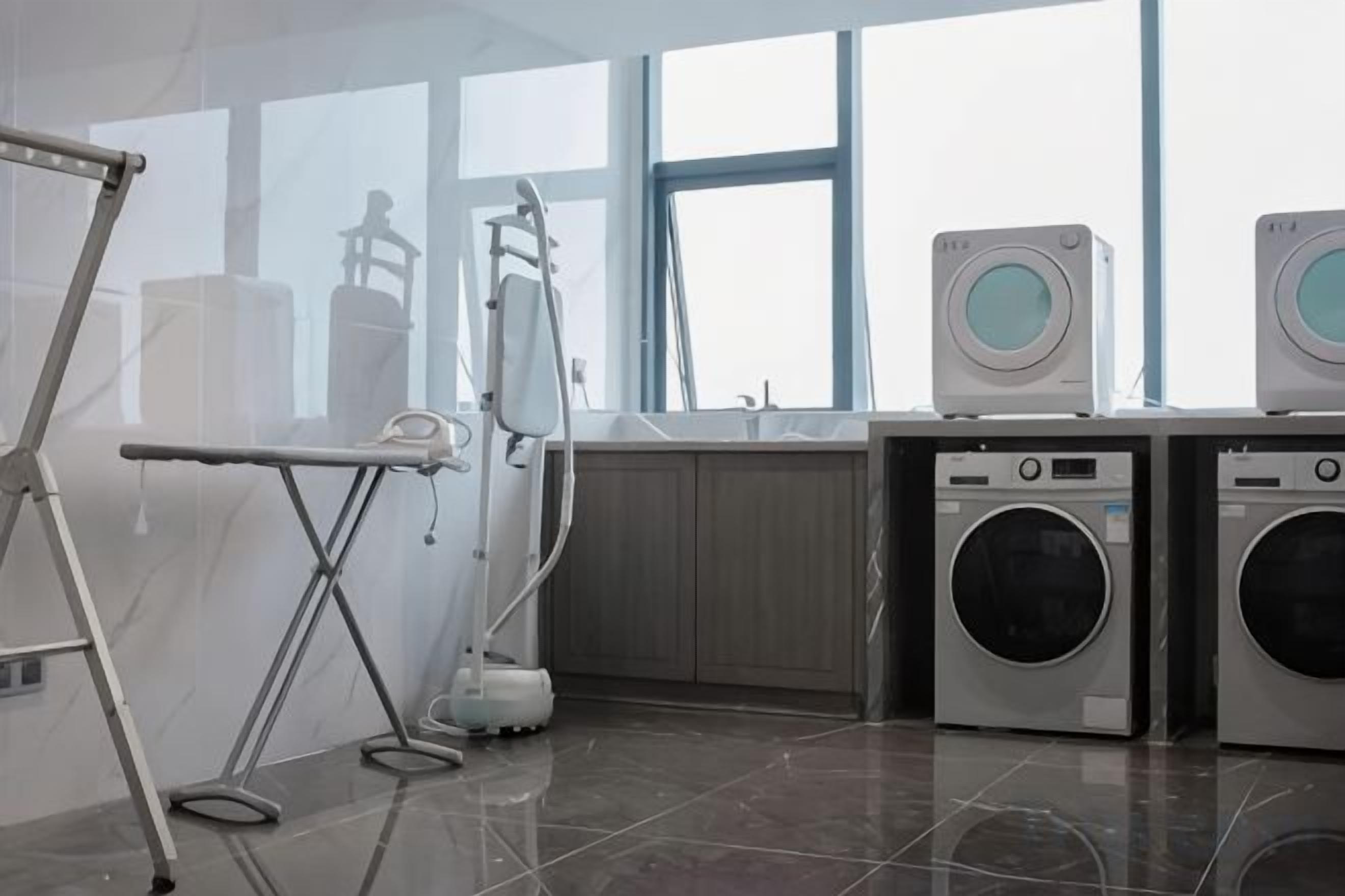 A laundry facility with industrial washing machines, a drying rack, and a large window providing natural light.