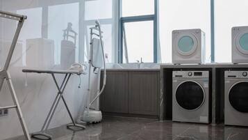 A laundry facility with industrial washing machines, a drying rack, and a large window providing natural light.