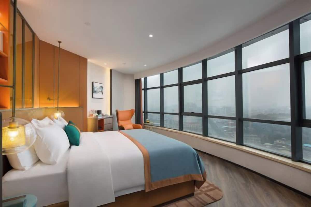 Ein modernes Hotelzimmer mit einem großen Bett, einem Nachttisch, einem Sessel und einem großen Fenster mit Blick auf die Stadt.