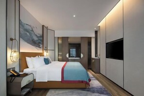 Une chambre d’hôtel moderne, dotée d’un grand lit, d’une télévision, d’un bureau avec un téléphone et d’un tableau au mur.