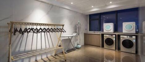 A laundry area with a drying rack, two washing machines, and a folding station.