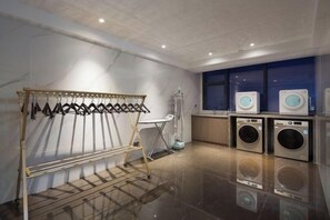 A laundry area with a drying rack, two washing machines, and a folding station.