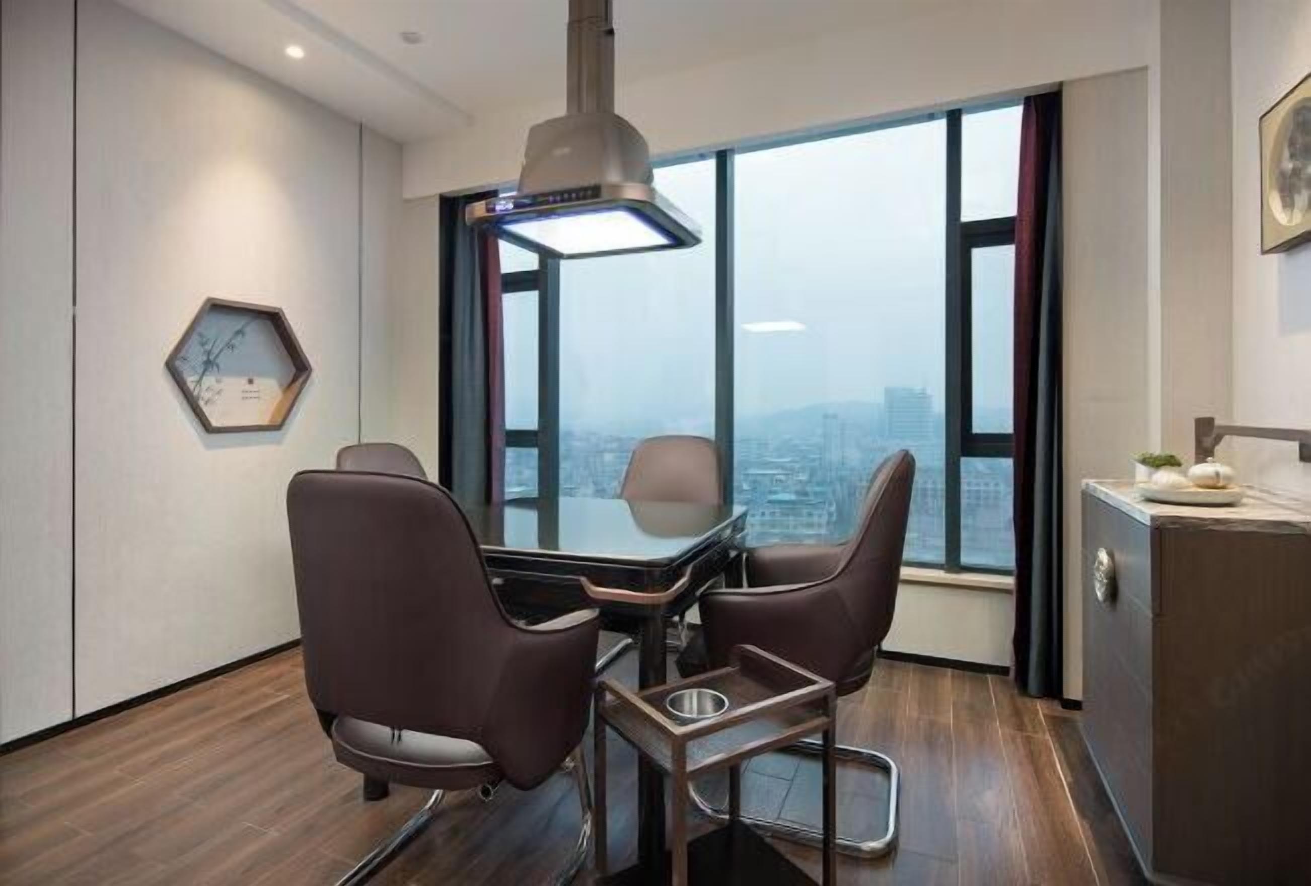 Un espacio de oficina moderno con una mesa de conferencias, dos sillas, una lámpara colgante, un reloj hexagonal y vistas de la ciudad a través de amplios ventanales.