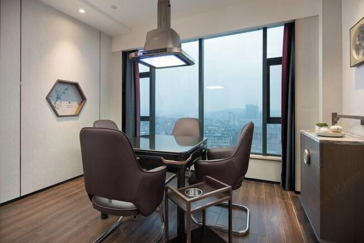 Un espace de bureau moderne comprenant une table de conférence, deux chaises, un luminaire suspendu, une horloge hexagonale et une vue sur la ville à travers de grandes fenêtres.