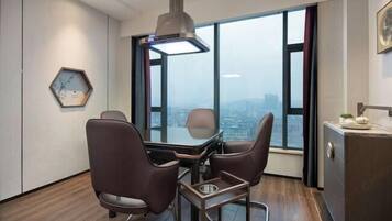 Un espacio de oficina moderno con una mesa de conferencias, dos sillas, una lámpara colgante, un reloj hexagonal y vistas de la ciudad a través de amplios ventanales.