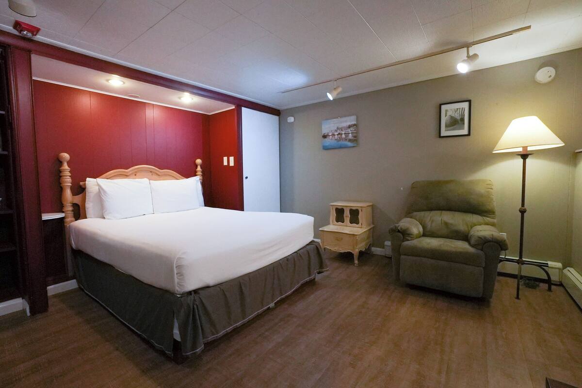 Une chambre d’hôtel avec un lit, une chaise, une table de chevet et une lampe.