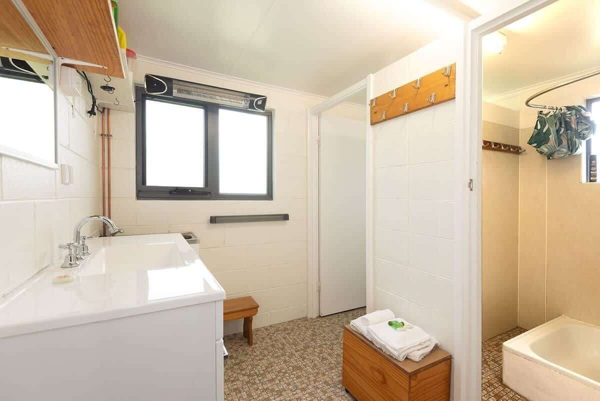 Un bany amb un lavabo blanc, una finestra, una dutxa i una banca de fusta.