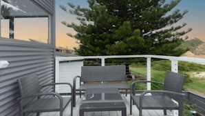 A deck with a metal railing, two wicker chairs, and a small table. - Jenkins Galwad-y-Mor | Beachfront Tomakin (TOMAKIN)