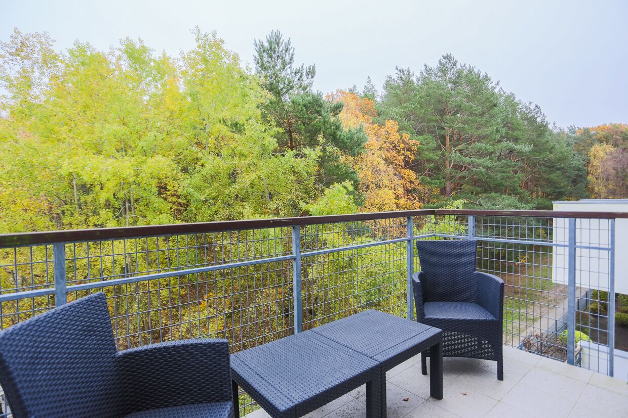 A balcony with wicker furniture and a view of autumn trees.