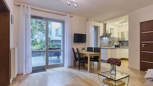Una sala de estar moderna con comedor, una cocina al fondo y un gran ventanal corredizo que da a un balcón.