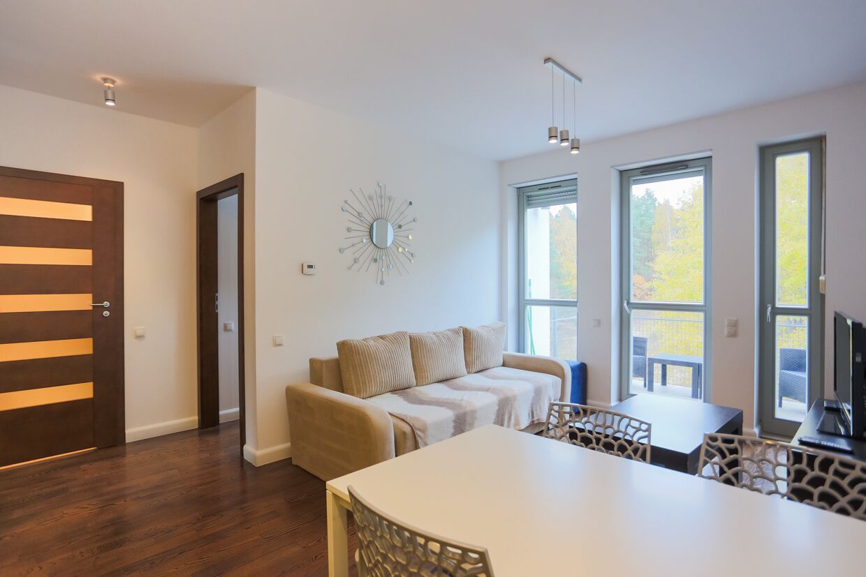 Un salon moderne avec un canapé, une table à manger et des chaises. Il y a de grandes fenêtres et un luminaire au plafond.