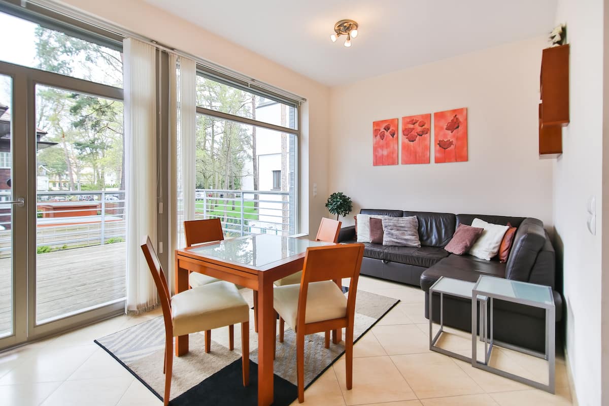 A modern living room with a glass dining table, two chairs, a sofa, and a small side table.