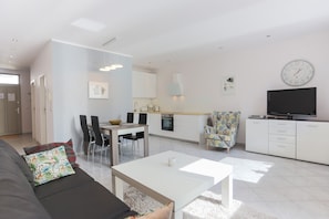 Un salon moderne comprenant un canapé, une table basse et un coin repas avec des chaises et une table. Il y a également un coin cuisine avec des placards et un téléviseur.