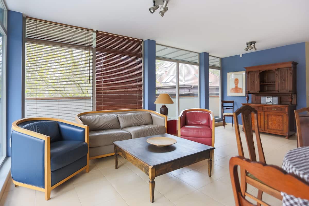 A living room with a sofa, armchair, coffee table, and a dining table with chairs.
