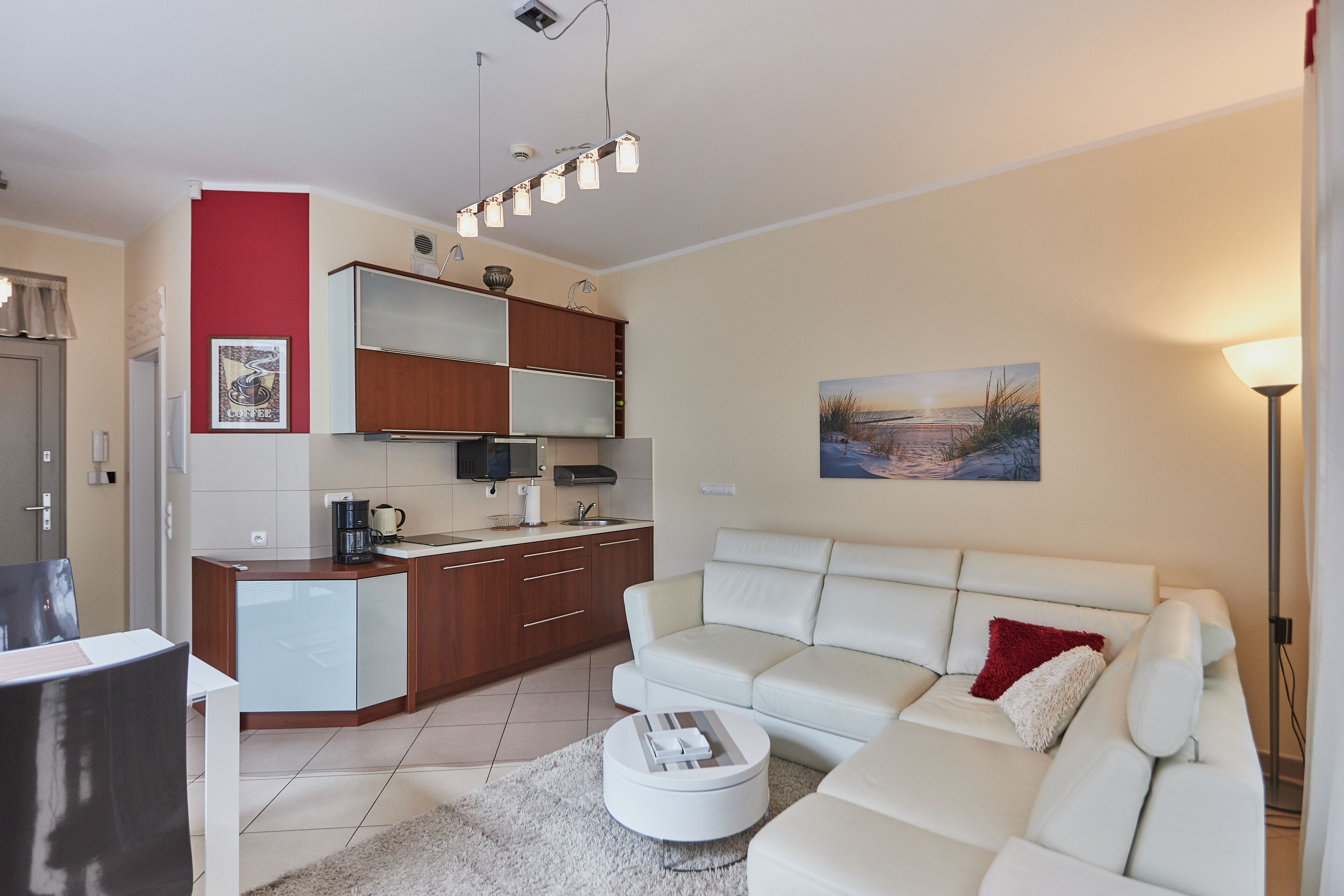 Una sala de estar moderna con un sofá blanco, una mesa de centro y una zona de cocina con armarios de madera y un microondas.