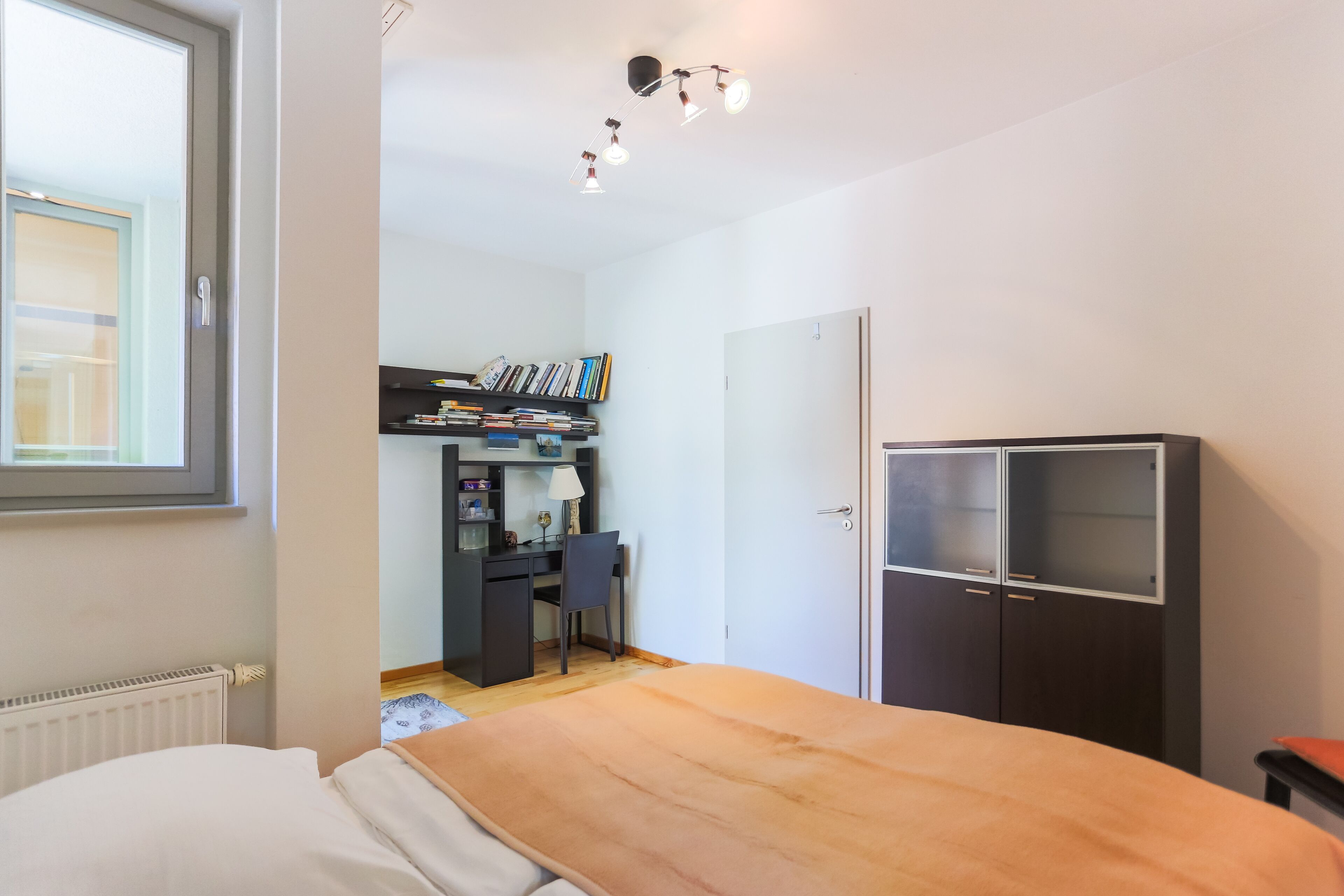 Quarto com cama, escrivaninha, cadeira, guarda-roupa e radiador.