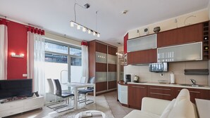 A modern living room with a flat-screen TV, white sofa, and a dining area with a table and chairs. - Apartamenty Swinoujscie - Marinos (Swinoujscie)