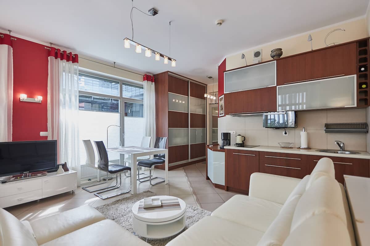 A modern living room with a flat-screen TV, white sofa, and a dining area with a table and chairs.