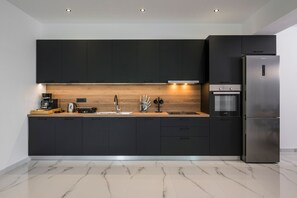 A modern kitchen with dark cabinets, a wooden countertop, a stainless steel refrigerator, and a built-in oven.
