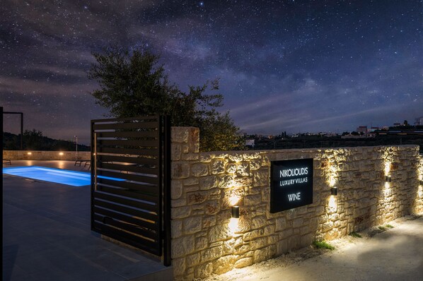 A stone wall with a sign for Nikolioudis Luxury Villas and a pool area.