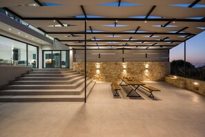 A modern outdoor patio with a stone wall, a wooden bench, and a table.