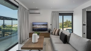 Un salon moderne doté d’un grand téléviseur à écran plat, d’un canapé, d’une table basse et offrant une vue sur la ville grâce à de grandes fenêtres.