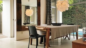 Uma sala de jantar moderna com uma mesa de madeira, cadeiras pretas, um espelho grande e um lustre.