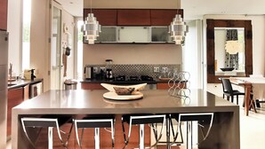 Uma cozinha moderna com ilha central, luminárias pendentes e área de refeições com cadeiras.