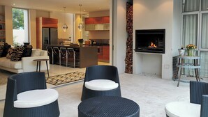 Uma cozinha moderna com TV integrada e lareira, área de refeições com banquetas de bar e um espaço de estar com cadeiras de vime.