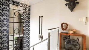 Um interior moderno com parede estampada, uma decoração de cabeça de touro, mesa consola de madeira com objetos decorativos e escada com corrimão de metal.