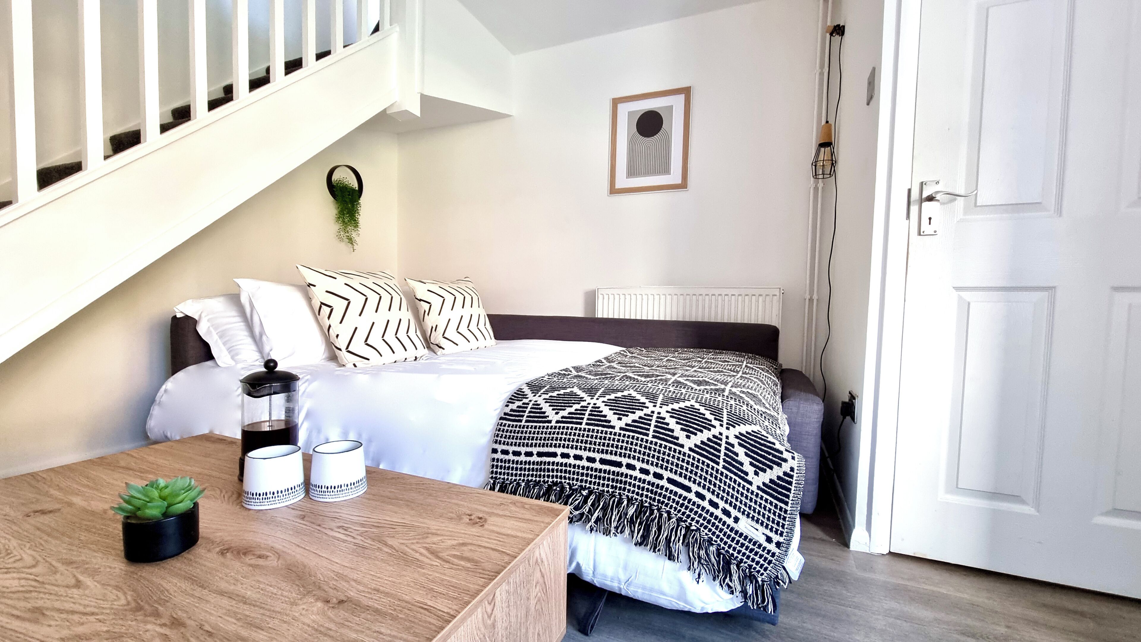 Een slaapkamer met een bed, nachtkastje met een plant, een radiator en een deur.