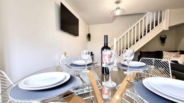 A dining area with a glass table set for four, a bottle of wine, and a staircase in the background. - Haxby House by Switchback Stays (Cardiff)